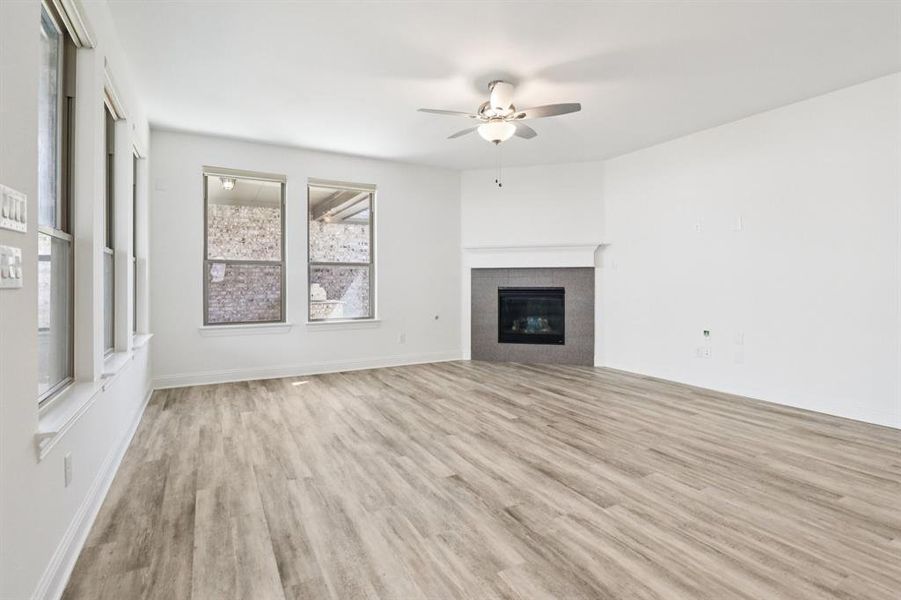 Unfurnished living room with light wood-type flooring, a tiled fireplace, and a ceiling fan Unfurnished living room with light wood-type flooring, a tiled fireplace, and a ceiling fan