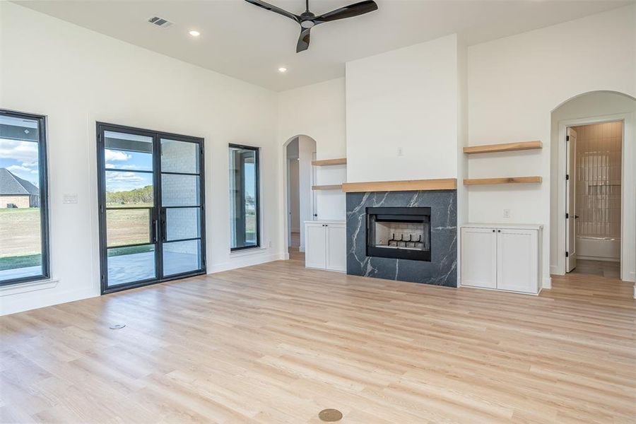 Unfurnished living room with a high ceiling, light wood-type flooring, ceiling fan, and a premium fireplace