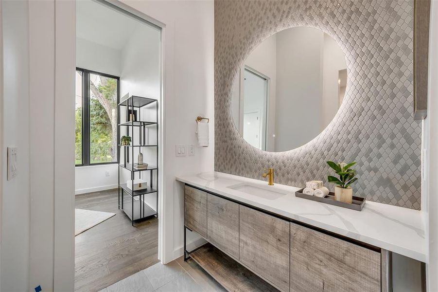 Guest bathroom boasts designer tile, a chic vanity, and a backlit mirror for a spa-like feel.