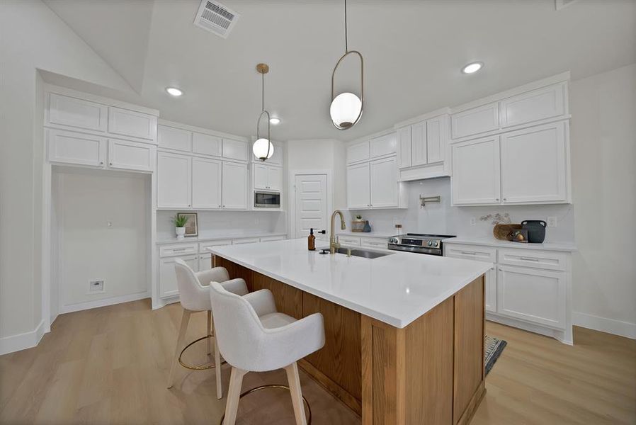 Kitchen featuring brown cabinetry, white cabinets, light wood finished floors, an island with sink, and recessed lighting Kitchen featuring brown cabinetry, white cabinets, light wood finished floors, an island with sink, and recessed lighting