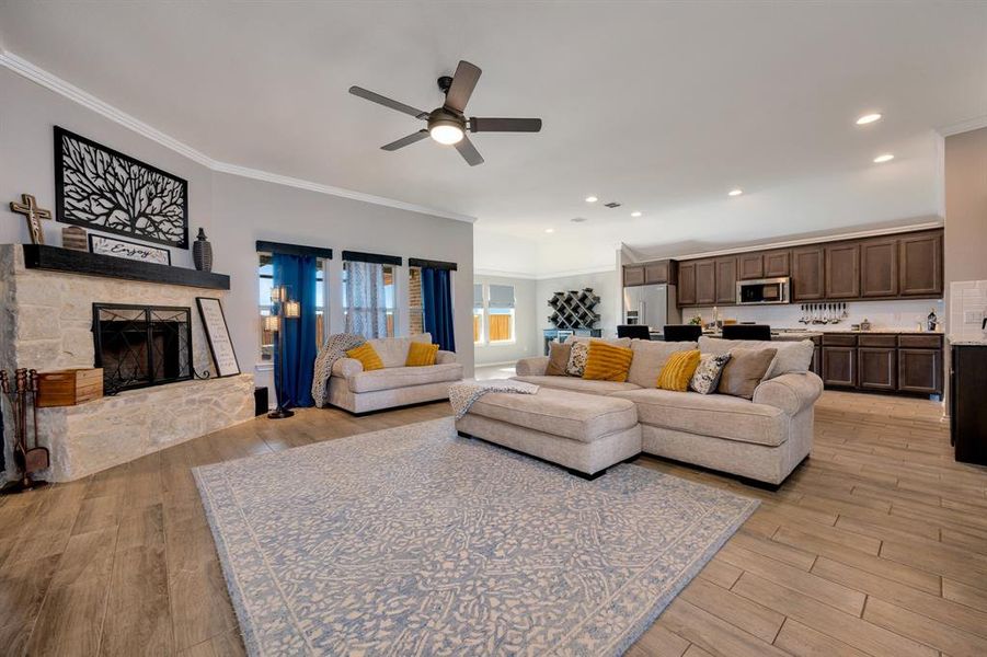 Living room featuring light wood-style flooring, crown molding, a fireplace, recessed lighting, and a ceiling fan