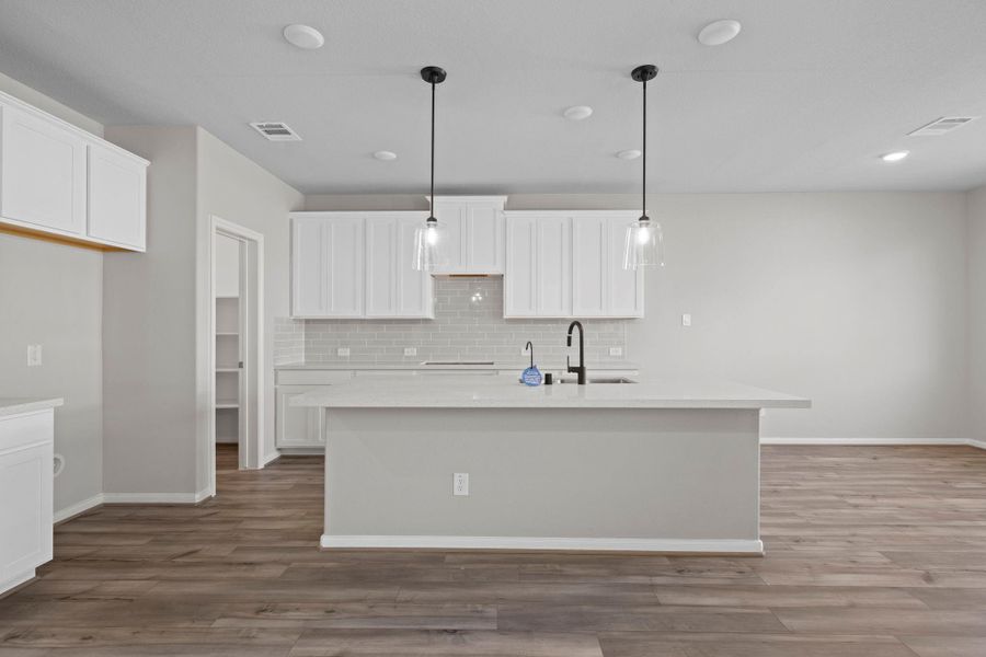 This light and bright kitchen features a large quartz island, white cabinets, a large sink overlooking your family room, recessed lighting, and beautiful backsplash.