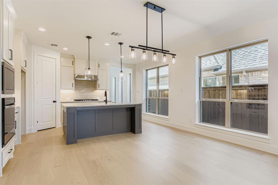 Kitchen featuring white cabinets, light wood finished floors, stainless steel oven, decorative backsplash, and light countertops Kitchen featuring white cabinets, light wood finished floors, stainless steel oven, decorative backsplash, and light countertops