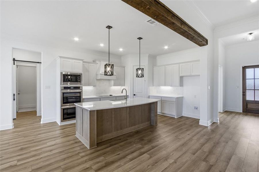 Dual tone kitchen featuring dual tone cabinets, an island with sink, pendant lighting, ornamental molding, and light wood finished floors