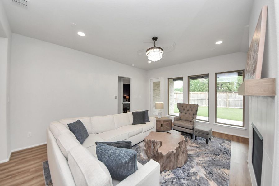 This spacious living room features a cozy sectional sofa, a stylish wood slab coffee table, and large windows offering plenty of natural light and views of the backyard. A contemporary chandelier and neutral decor create an inviting atmosphere.