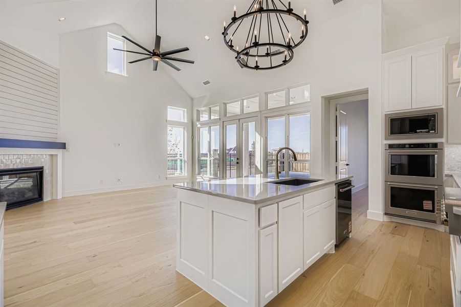 Kitchen featuring white cabinets, high vaulted ceiling, open floor plan, a chandelier, and a center island with sink Kitchen featuring white cabinets, high vaulted ceiling, open floor plan, a chandelier, and a center island with sink