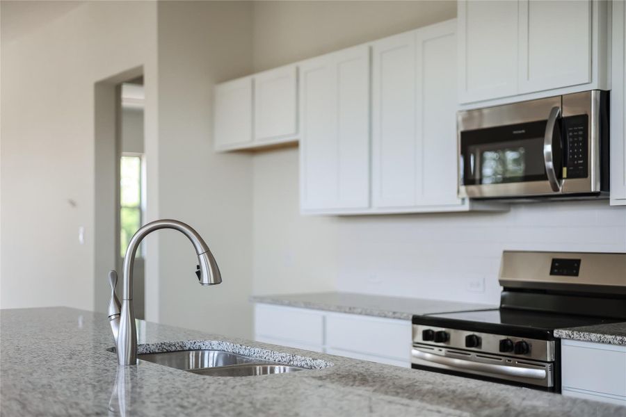 Kitchen featuring stainless steel appliances, white cabinetry, and light stone countertops