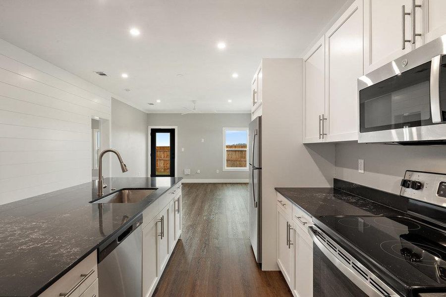 Kitchen with stainless steel appliances, dark quartz countertops, white cabinets, dark wood-type flooring, and recessed lighting.  "Silver" interior package pictured here