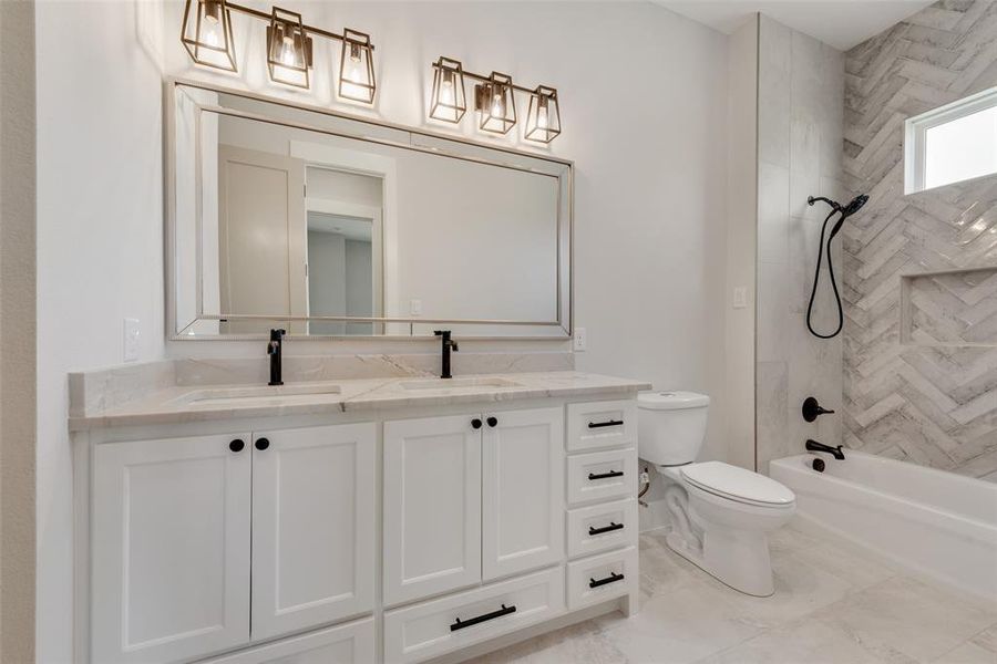 Full bathroom with dual vanity, tile flooring, toilet, and tiled shower / bath