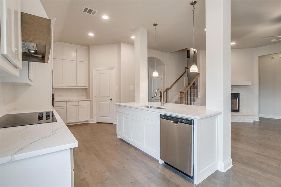 Kitchen with a fireplace, white cabinetry, light hardwood / wood-style flooring, decorative light fixtures, and dishwasher