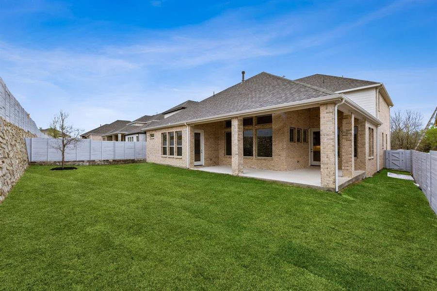 Rear view of house with a shingled roof, brick siding, a fenced backyard, and a patio