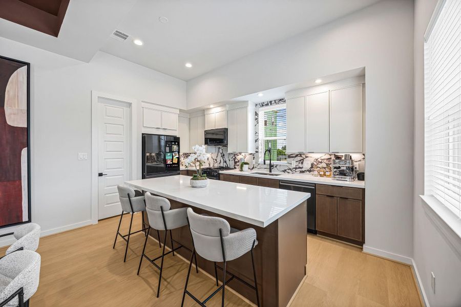 A modern kitchen featuring sleek cabinetry, a spacious island with seating, and stylish countertops, perfect for both casual dining and entertaining. **Model of similar home**