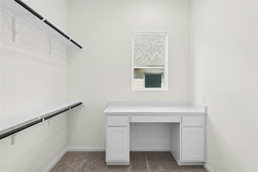 Walk in closet with built in study area and dark colored carpet Walk in closet with built in study area and dark colored carpet