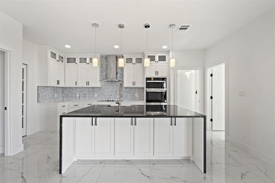 Kitchen with a kitchen island with sink, wall chimney exhaust hood, white cabinetry, and stainless steel double oven