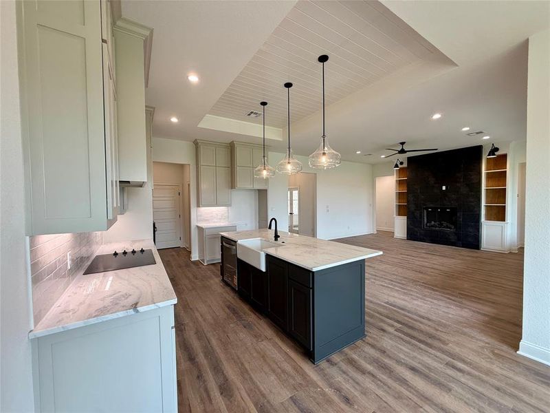 Dual tone kitchen with light stone counters, a fireplace, open floor plan, a kitchen island with sink, and built in features