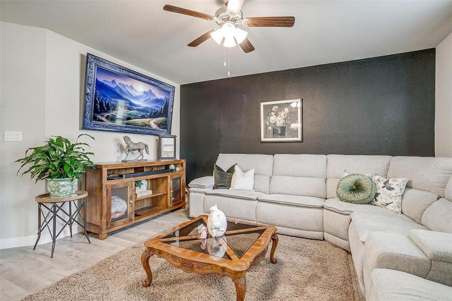 Living area featuring ceiling fan, an accent wall, baseboards, and wood finished floors