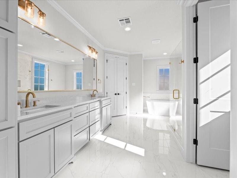 Full bathroom with double vanity, ornamental molding, a freestanding tub, recessed lighting, and light marble finish floors