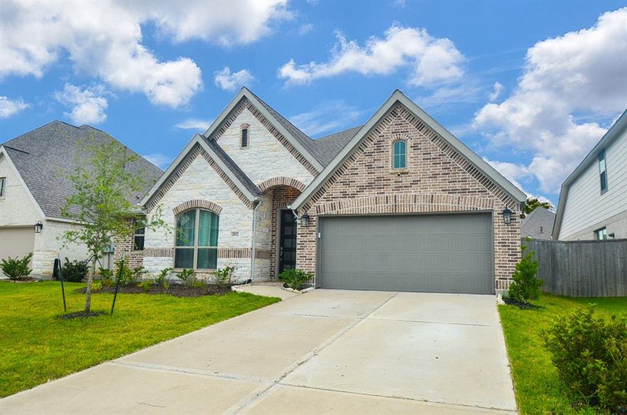 The photo showcases a modern single-story brick home with an arched entryway, a two-car garage, and a well-maintained lawn.