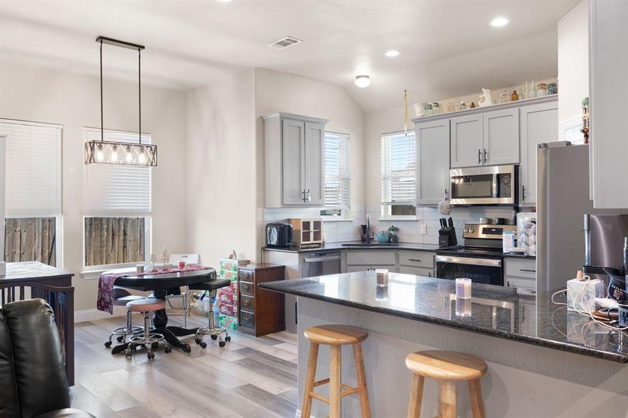 Kitchen featuring backsplash, dark stone counters, light hardwood / wood-style flooring, appliances with stainless steel finishes, and decorative light fixtures