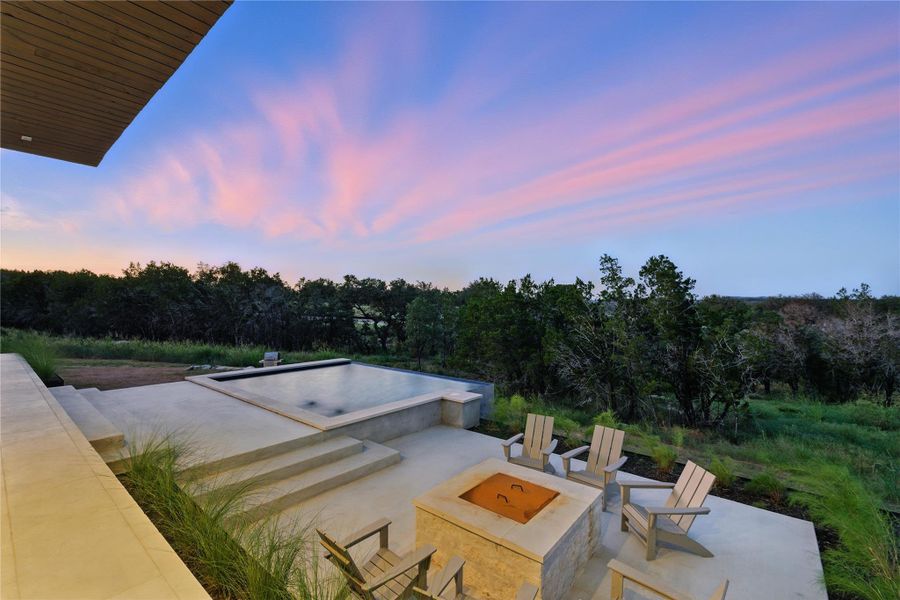 Patio terrace at dusk with a patio area, a fire pit, and a wooded view