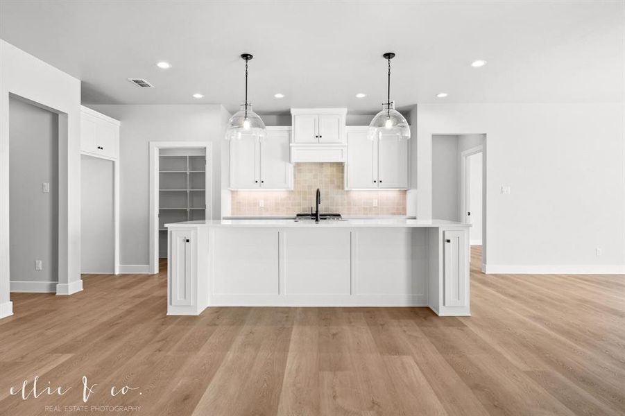 Kitchen featuring white cabinets, an island with sink, tasteful backsplash, decorative light fixtures, and recessed lighting
