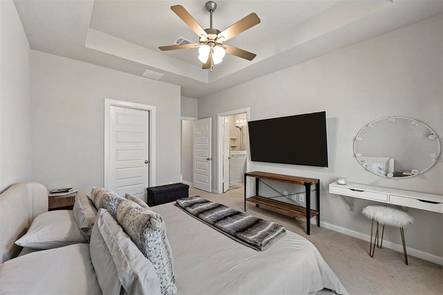 Bedroom with light colored carpet, a tray ceiling, ceiling fan, and ensuite bath Bedroom with light colored carpet, a tray ceiling, ceiling fan, and ensuite bath