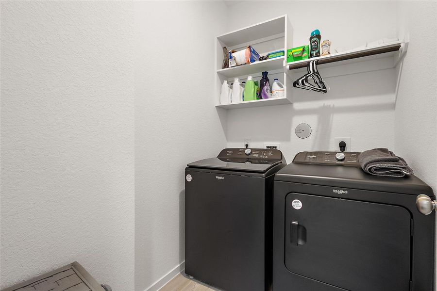 This is a compact, well-organized laundry room featuring a modern washer and dryer set, wall-mounted shelving for storage, and a hanging rod for clothes.
