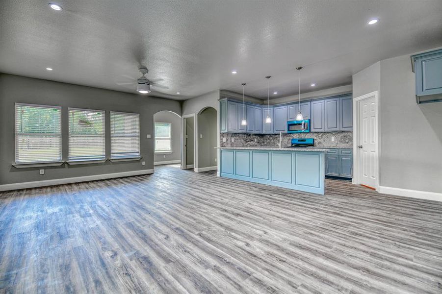 Kitchen with backsplash, ceiling fan, range, wood-type flooring, and pendant lighting