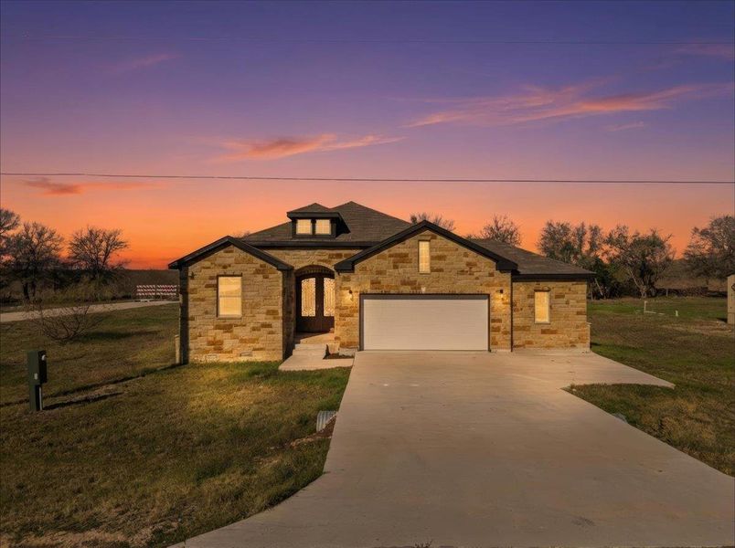 View of front of home with driveway, a front lawn, stone siding, and a garage View of front of home with driveway, a front lawn, stone siding, and a garage