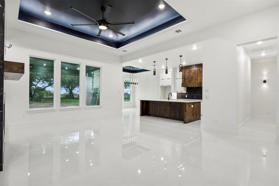 Kitchen featuring light tile patterned floors, dark brown cabinets, a raised ceiling, a center island, and pendant lighting