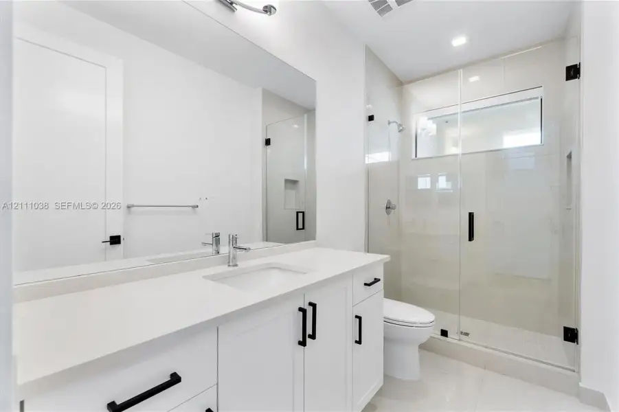 White cabinetry vanity with solid surface countertop, glass-enclosed shower with tiled walls and built-in niche, and matte black hardware fixtures
