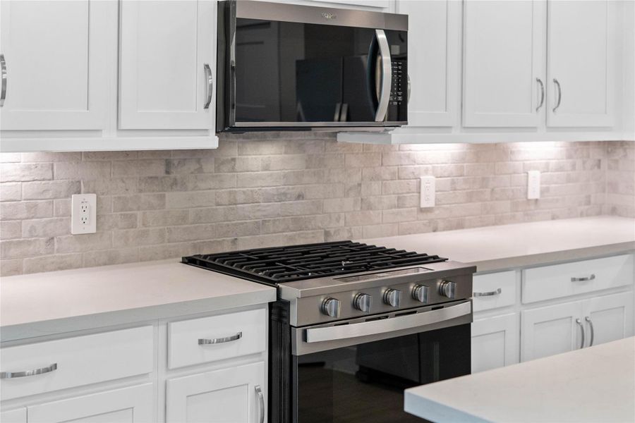 Showcased here is a Whirlpool gas range with center oval burner, paired with a steam microwave equipped with sensor cooking—all framed by an elegant tile backsplash.