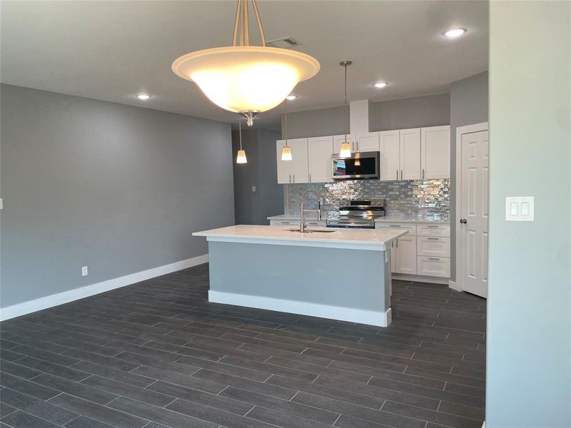 Kitchen featuring sink, dark hardwood / wood-style flooring, hanging light fixtures, white cabinetry, and stainless steel appliances