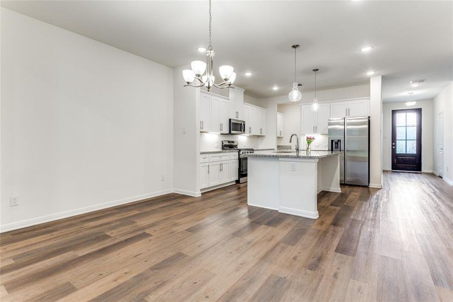 Kitchen featuring a center island with sink, stainless steel appliances, light stone countertops, hardwood / wood-style flooring, and white cabinets