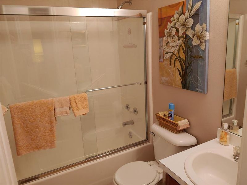 Full bathroom featuring a shower-tub combination with sliding glass doors, a single vanity with an integrated sink, and a commode