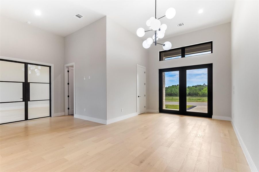 Entryway featuring a high ceiling, a chandelier, light wood-type flooring, and baseboards Entryway featuring a high ceiling, a chandelier, light wood-type flooring, and baseboards