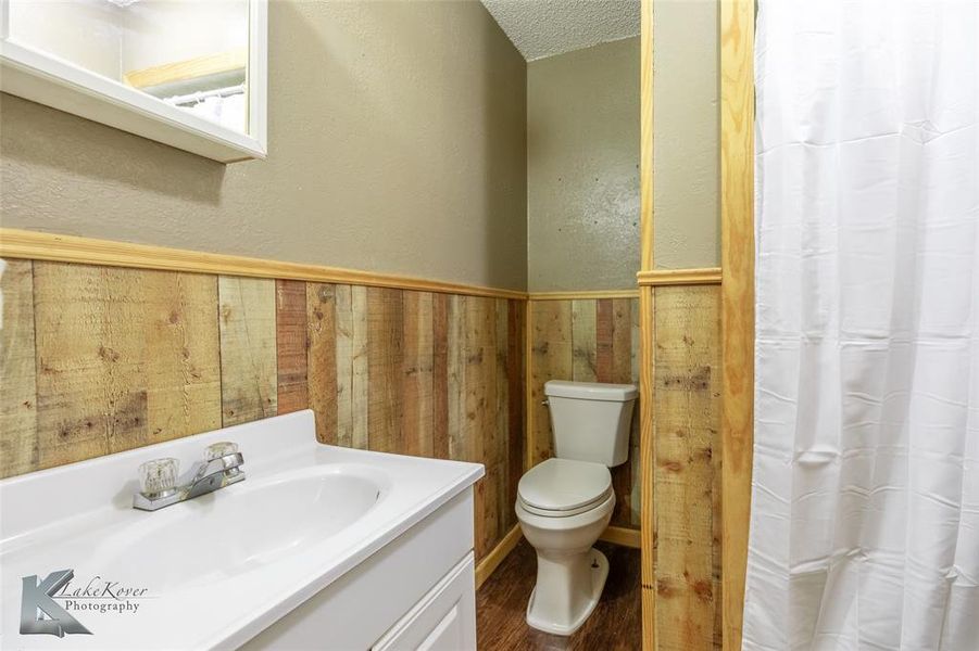 Bathroom featuring vanity, wood finished floors, a textured ceiling, a textured wall, and a shower with shower curtain