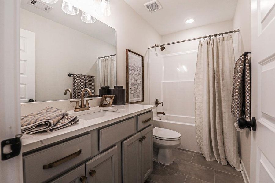 Full bathroom with vanity, shower / bath combination with curtain, and dark tile patterned flooring