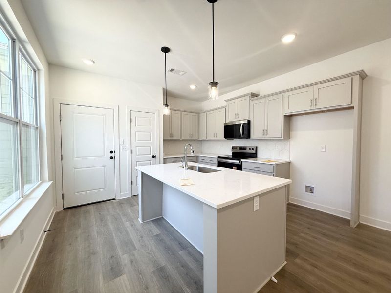 Kitchen featuring stainless steel appliances, gray cabinetry, light stone countertops, and a kitchen island with sink