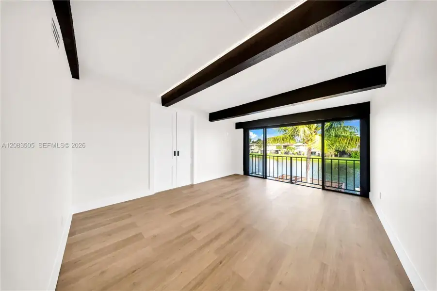 Wood-finish flooring, exposed ceiling beams, and dual sliding glass doors opening to a waterfront balcony Wood-finish flooring, exposed ceiling beams, and dual sliding glass doors opening to a waterfront balcony