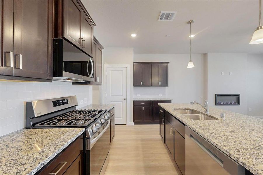 Kitchen featuring appliances with stainless steel finishes, light stone countertops, dark brown cabinets, recessed lighting, and a glass covered fireplace