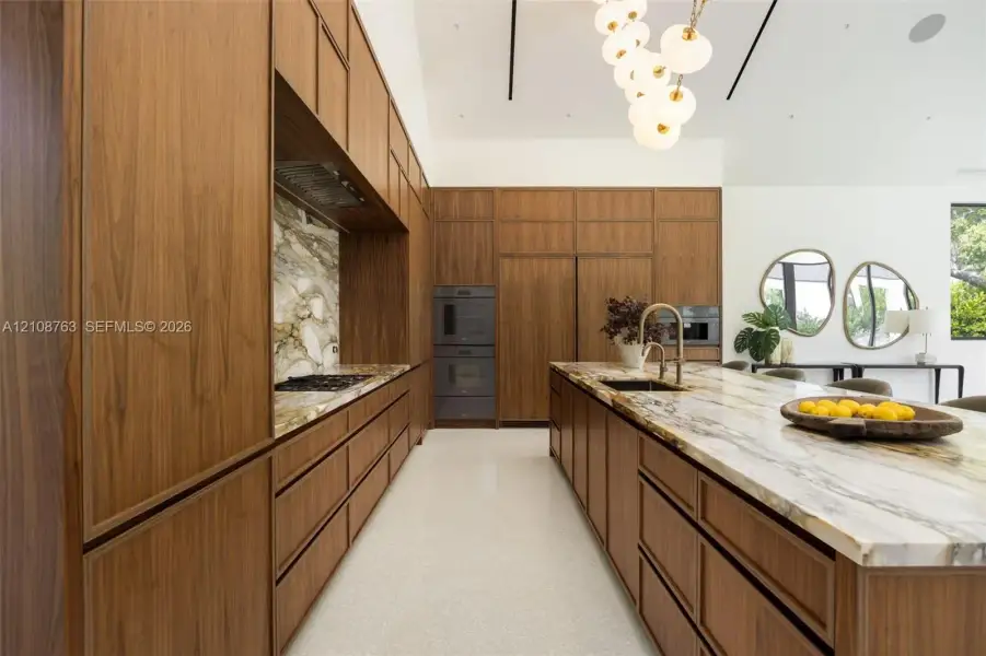 Custom wood-finish cabinetry, natural stone countertops and backsplash, integrated double wall ovens, terrazzo flooring, and a multi-globe pendant light fixture
