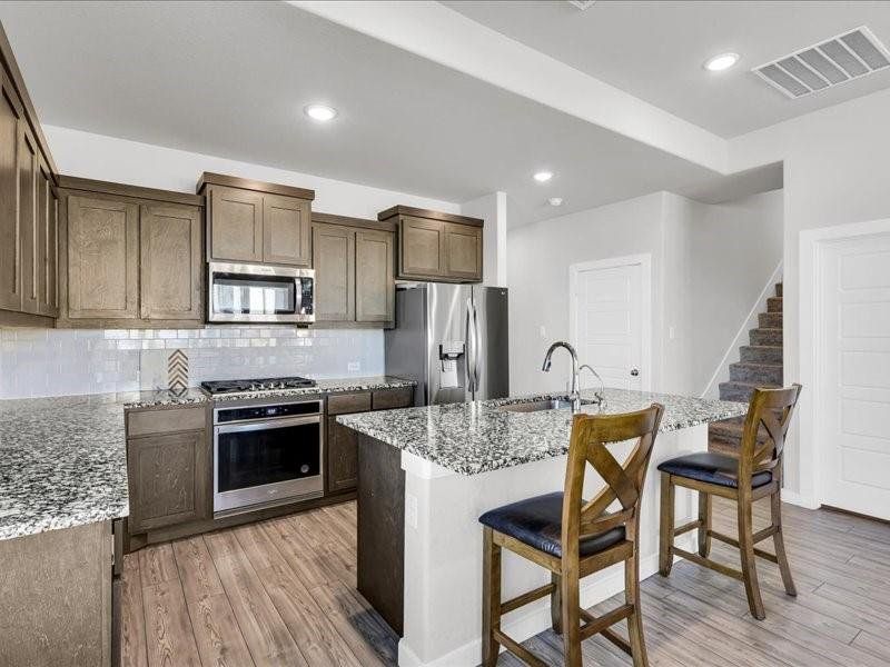 Kitchen featuring sink, light stone counters, a kitchen bar, a center island with sink, and appliances with stainless steel finishes