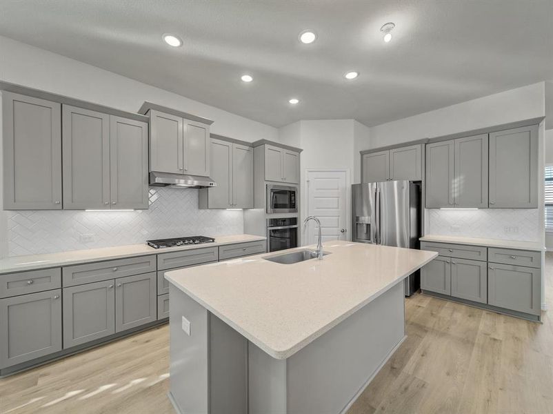 Kitchen featuring gray cabinetry, a center island with sink, and stainless steel appliances