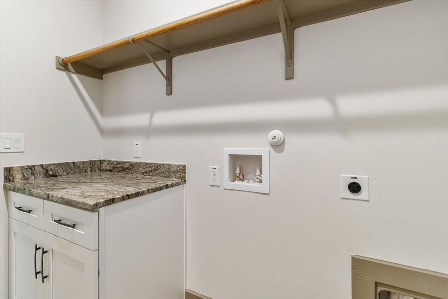 Laundry room with cabinet space and granite countertop. Shelving above