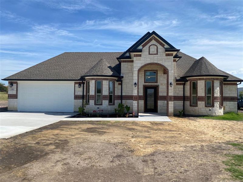 French country inspired facade featuring stone siding, roof with shingles, concrete driveway, and a garage French country inspired facade featuring stone siding, roof with shingles, concrete driveway, and a garage