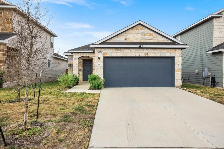 French country inspired facade featuring stone siding, concrete driveway, a garage, and a front yard
