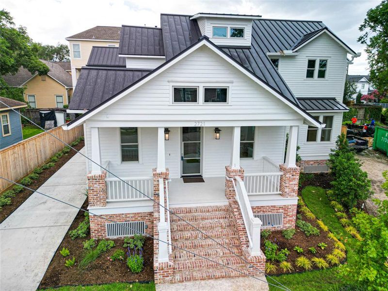 Aerial view of a white house with a striking brick entrance and a metal roof. A guy wire stretches across the front yard, to be removed.