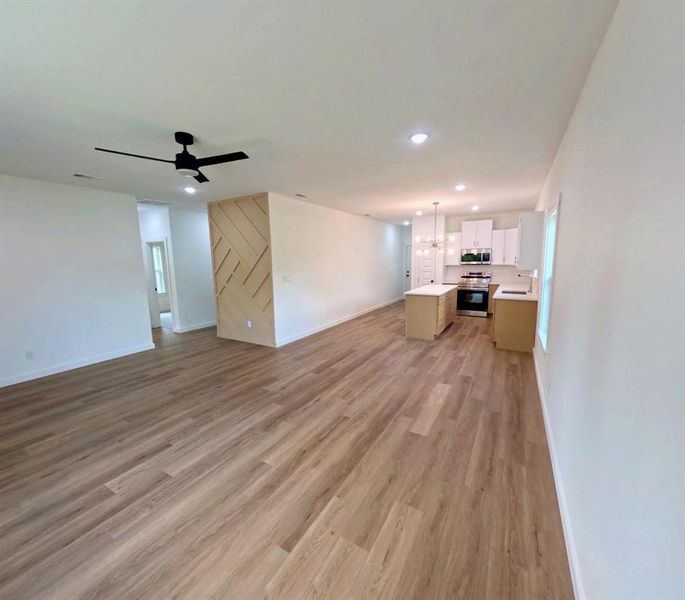 Unfurnished living room with light wood-style flooring, recessed lighting, a ceiling fan, and a chandelier Unfurnished living room with light wood-style flooring, recessed lighting, a ceiling fan, and a chandelier