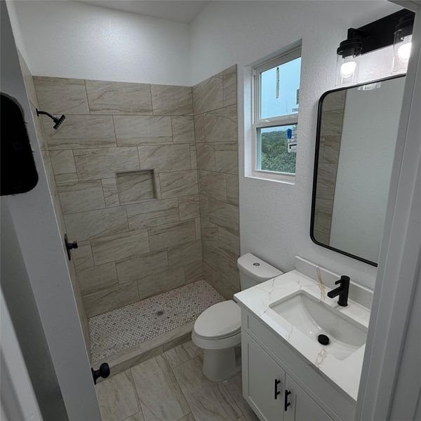 Modern bathroom featuring a walk-in shower with stone-look tile walls and a mosaic tile floor, white vanity with quartz countertop, rectangular undermount sink, and matte black fixtures